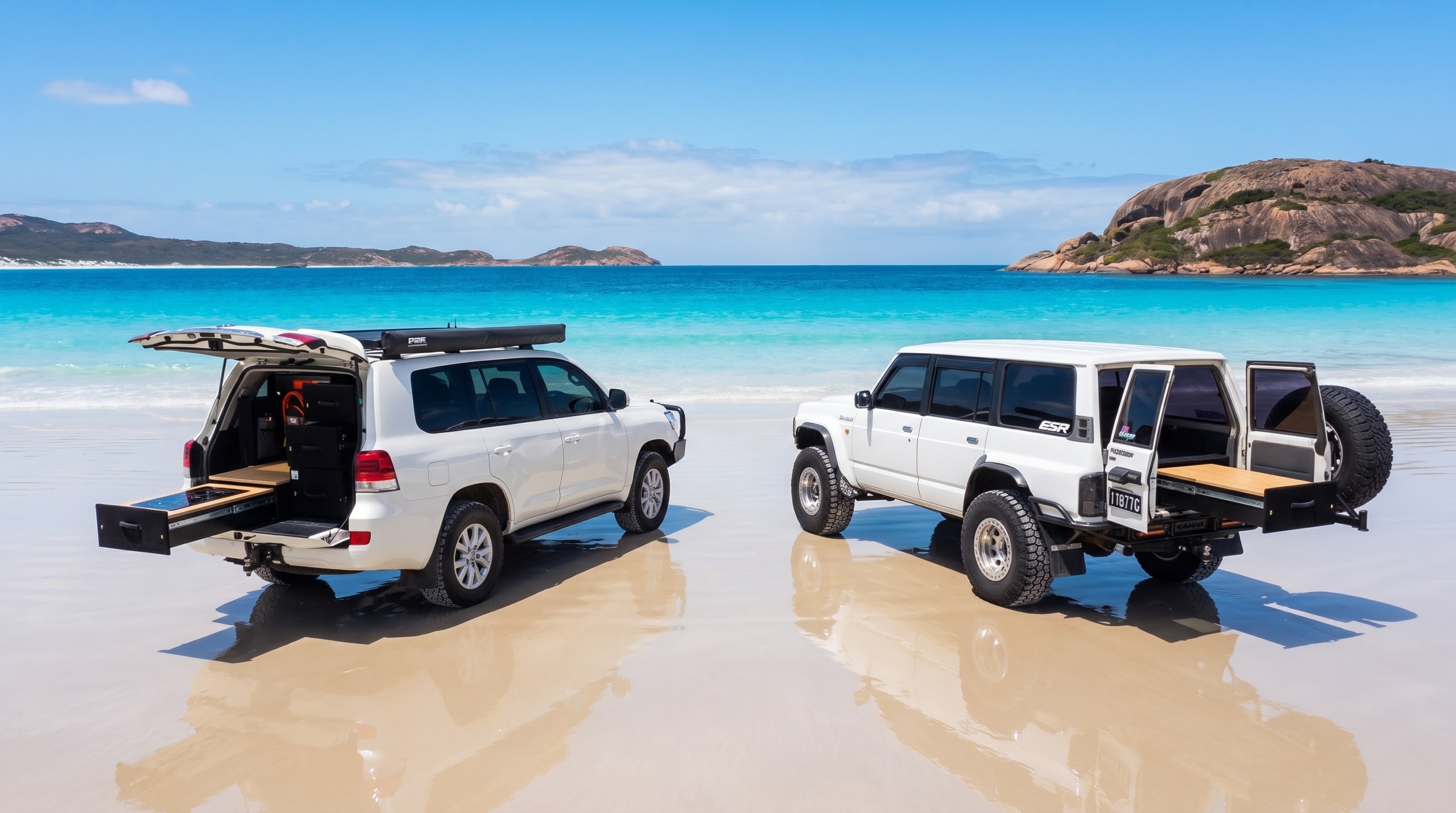 Two real Bandit Customs builds on Lucky Bay: a white LandCruiser touring fit-out with its drawer system slid out, and a GQ Patrol with its rear drawers open